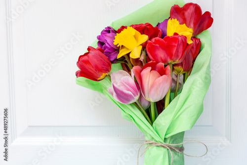 Fototapeta Naklejka Na Ścianę i Meble -  Bouquet of colorful tulips wrapped with green paper on white wooden  background 