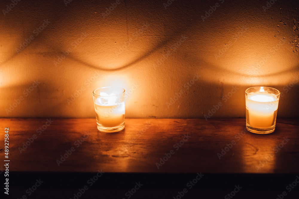 votive candles on wood shelf creating dramatic shadows on white brick wall - obrazy, fototapety, plakaty 