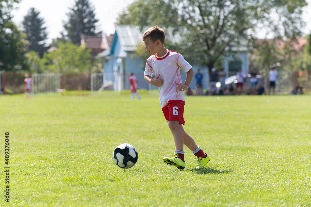 The little football player practicing his football skill alone at the playground.