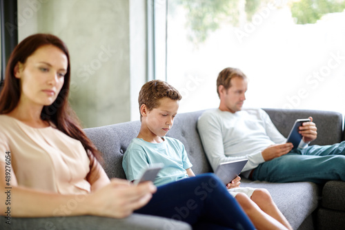 Left to their own devices.... Shot of a family of three sitting separately on a sofa with their own digital devices.