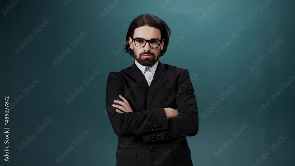 Fototapeta premium A handsome young man with long hair in a black suit and shirt taking on the eyeglasses