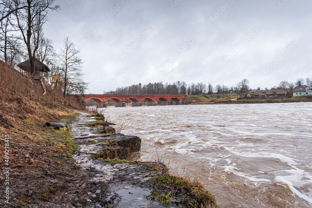 High water level in Venta river on spring day and old red brick bridge. Kuldiga, Latvia.