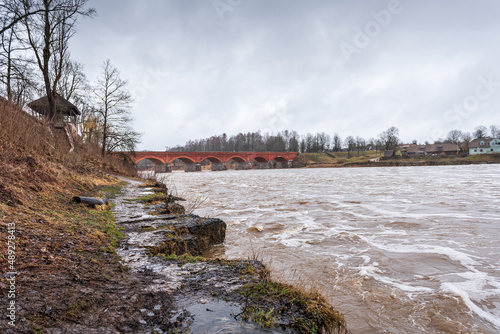 High water level in Venta river on spring day and old red brick bridge. Kuldiga, Latvia.