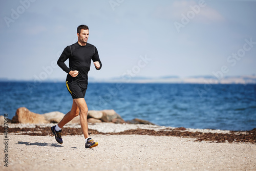 Running on the sand is a great workout. Shot of a handsome young man running on the beach.