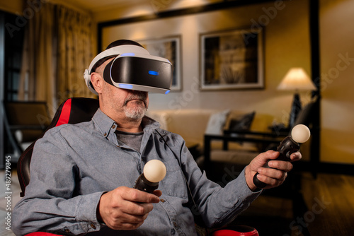 Hombre mayor disfrutando de sus juegos en realidad virtual en el living room de su casa photo