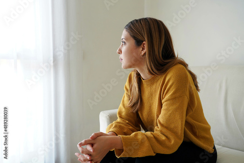 Murais de parede Melancholic sad woman looking through the window at home