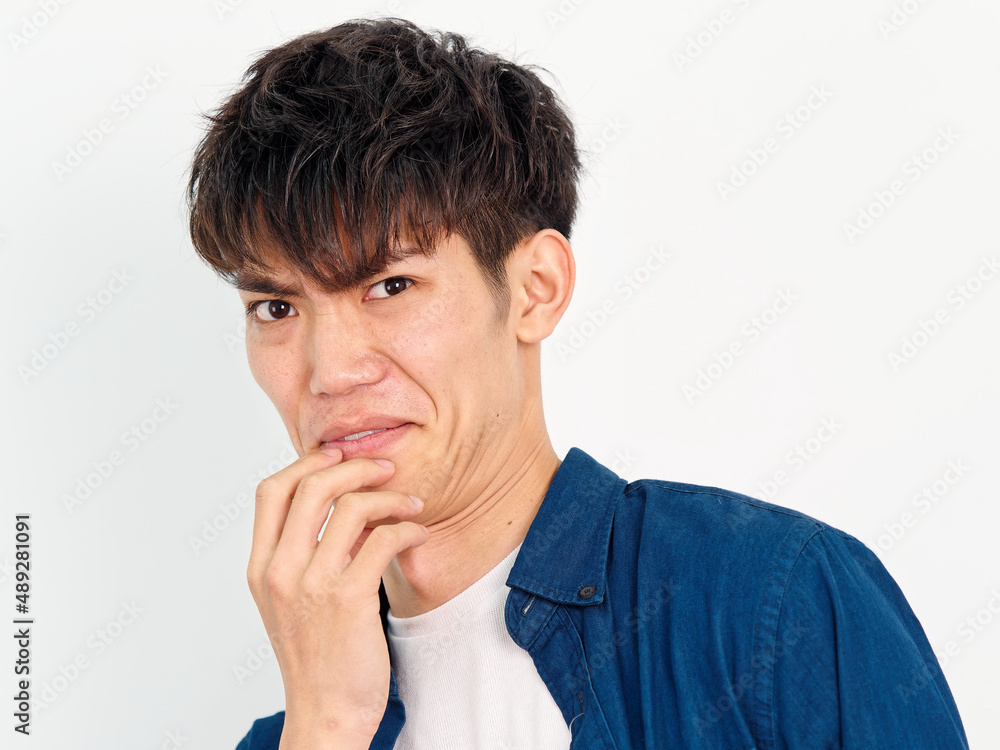 Portrait of handsome Chinese young man with curly black hair in blue shirt posing against white wall background. Hand on his mouth with disgusted expression, looks unhappy, front view. Portrait of handsome Chinese young man with curly black hair in blue shirt posing against white wall background. Hand on his mouth with disgusted expression, looks unhappy, front view.