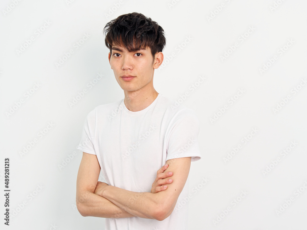 Portrait of handsome Chinese young man with curly black hair in white T-shirt posing against white wall background. Arms crossed and looking at camera, looks confident, front view. Portrait of handsome Chinese young man with curly black hair in white T-shirt posing against white wall background. Arms crossed and looking at camera, looks confident, front view.