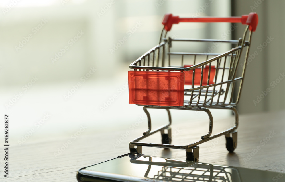 Close up shopping cart and mobile phone on wooden surface. Concept for money spending and financial background Close up shopping cart and mobile phone on wooden surface. Concept for money spending and financial background