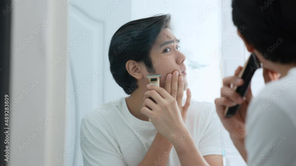 Health concept of 4k Resolution. Young Asian man shaving in the bathroom. look in the mirror. electric shaver. Health concept of 4k Resolution. Young Asian man shaving in the bathroom. look in the mirror. electric shaver.