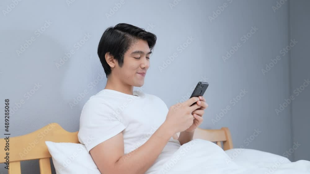 Holiday concept of 4k Resolution. Young Asian man playing mobile phone in bedroom. Holiday concept of 4k Resolution. Young Asian man playing mobile phone in bedroom.