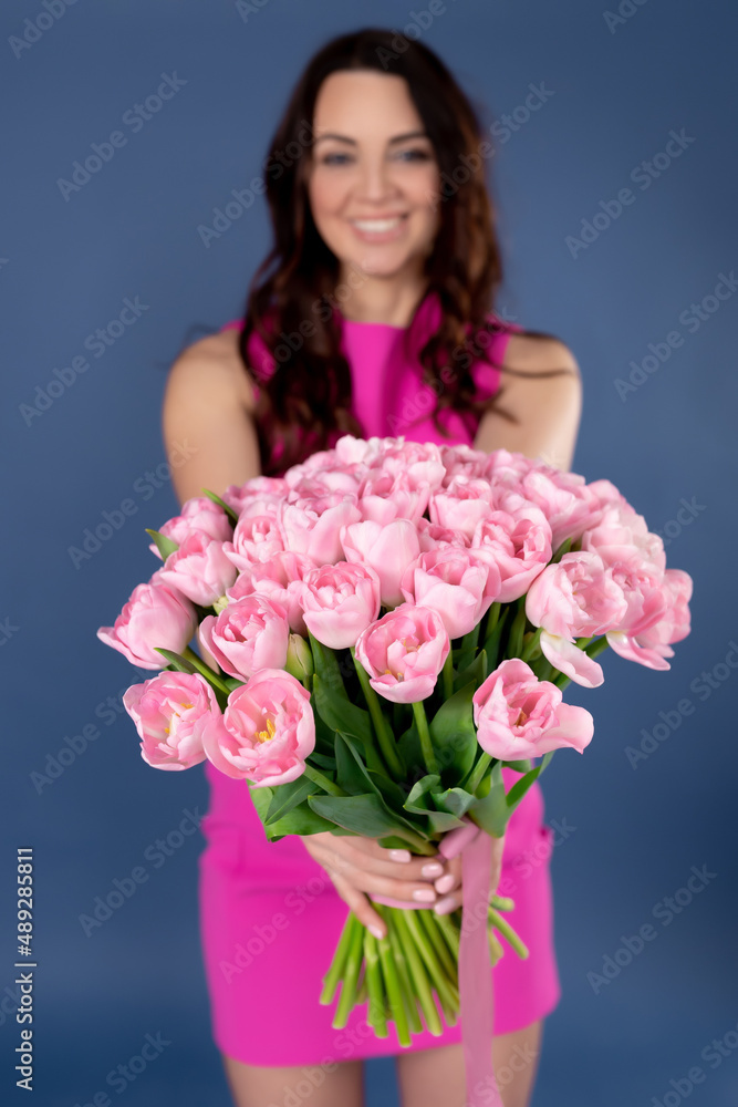A bouquet of pink tulips in the hands of a girl on a blue background. Bouquet of spring flowers in hands. The concept of mother's day, March 8, international women's day, business