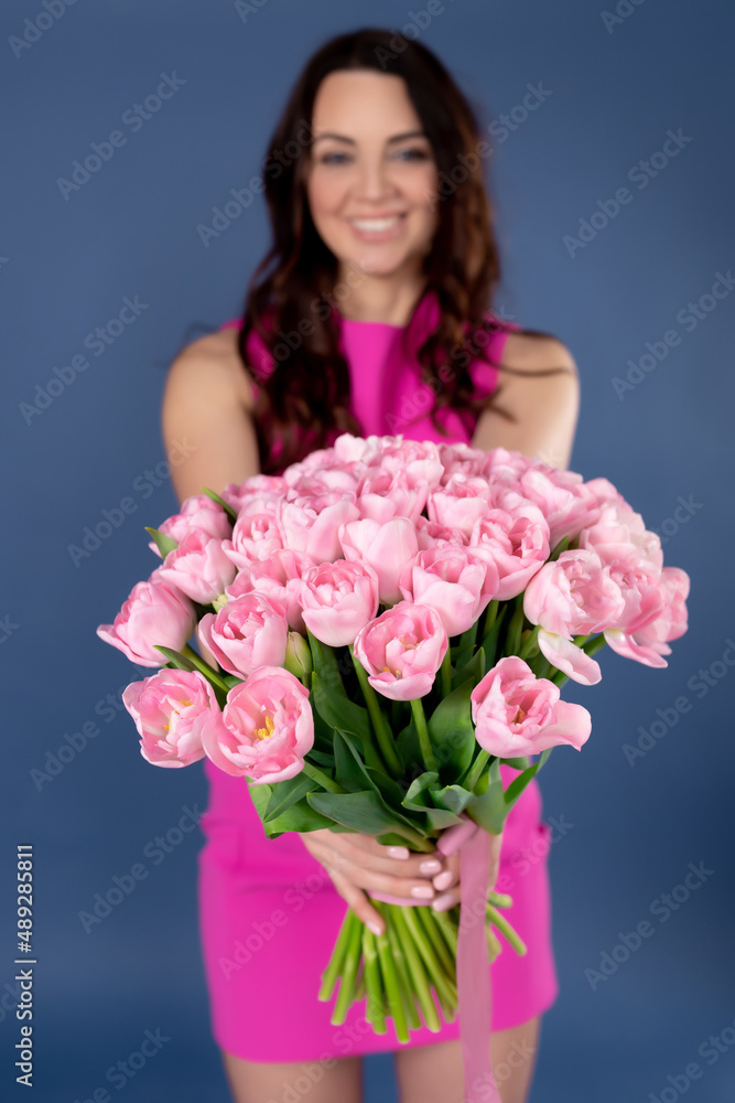 A bouquet of pink tulips in the hands of a girl on a blue background. Bouquet of spring flowers in hands. The concept of mother's day, March 8, international women's day, business A bouquet of pink tulips in the hands of a girl on a blue background. Bouquet of spring flowers in hands. The concept of mother's day, March 8, international women's day, business