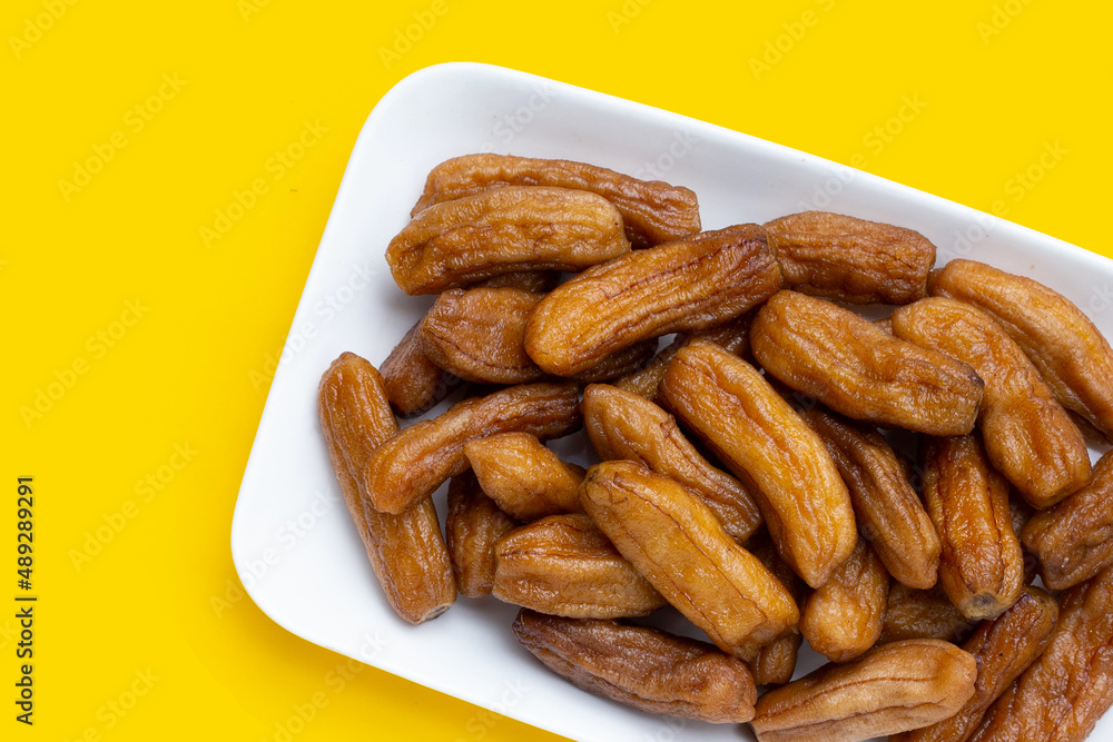 Fototapeta premium Sun-dried bananas in plate on yellow background.