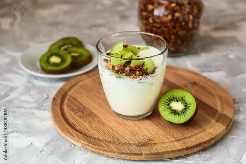 Breakfast: homemade granola and yogurt with fruit (kiwi) on a gray background.