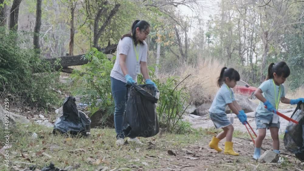 Group of Asian volunteer families collecting garbage and plastic by the river. Put garbage in the bin to help save the environment. World Environment Day