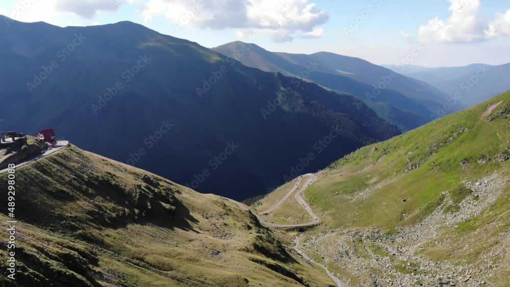 Aerial view, drone flying over Transfagarasan mountain in Romania. Winding roads in the middle of a valley, a lot of cars passing by. Beautiful day, clear white clouds. Huge mountains on background. Aerial view, drone flying over Transfagarasan mountain in Romania. Winding roads in the middle of a valley, a lot of cars passing by. Beautiful day, clear white clouds. Huge mountains on background.