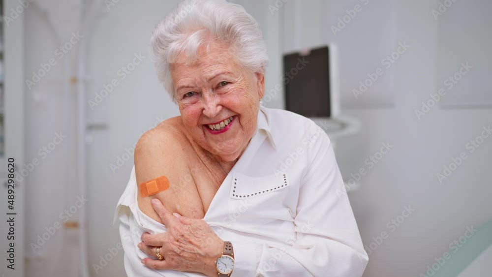 Happy senior woman showing bandage on arm after vaccination in doctor's office. Happy senior woman showing bandage on arm after vaccination in doctor's office.