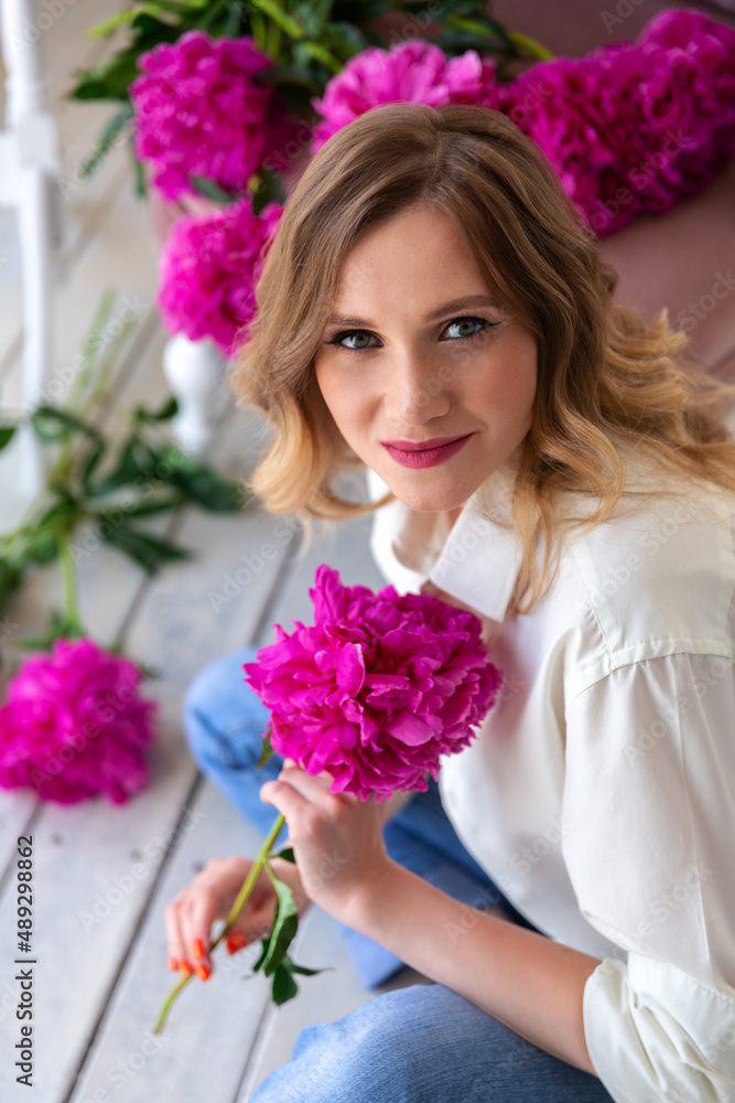 woman in shirt and jeans, holds bouquet of peonies in her hands, looks at camera and smiles. Portrait of beautiful blonde woman. Surprise bouquet of flowers for date, mothers day or valentines day woman in shirt and jeans, holds bouquet of peonies in her hands, looks at camera and smiles. Portrait of beautiful blonde woman. Surprise bouquet of flowers for date, mothers day or valentines day