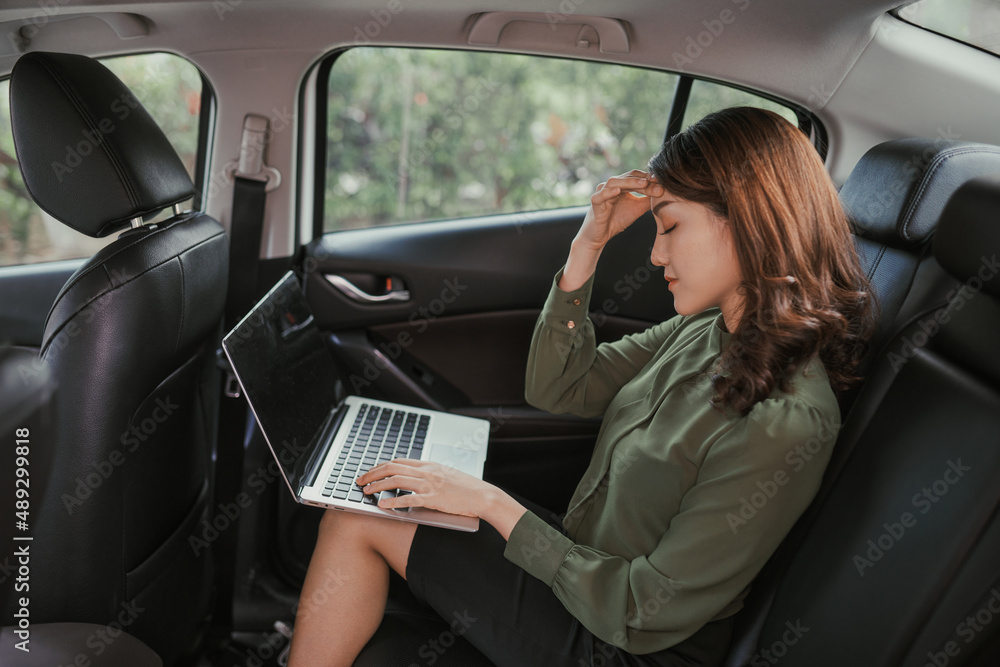 stressed young business woman using laptop computer while sitting in the back seat of car stressed young business woman using laptop computer while sitting in the back seat of car