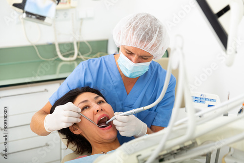 Professional dentist filling teeth for woman patient sitting in medical chair