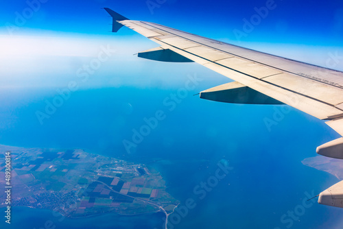 View from the airplane window at a beautiful blue clear sky, earth, sea and the airplane wing
