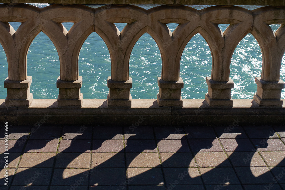 Fototapeta premium A shadow falls on the pavement from patterned balusters. A flowing turquoise river can be seen in the background.