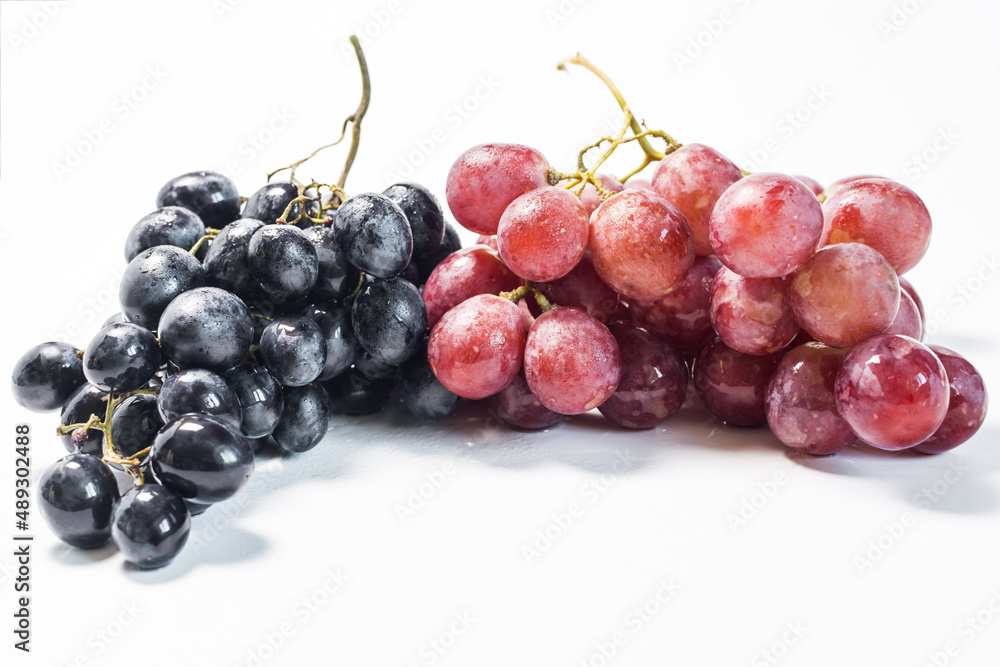 Branches of black and red grapes with water drops on a light background close-up.