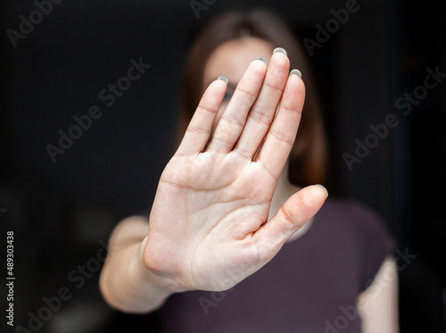 Close-up focus on a woman showing a stop gesture to the camera, blurred background, a strong young woman protesting against domestic violence and abuse, bullying, saying no to gender discrimination © Анатолий Савицкий