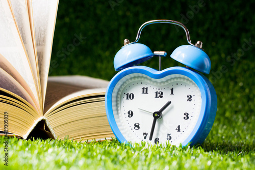 A blue heart-shaped alarm clock and a book on the grass