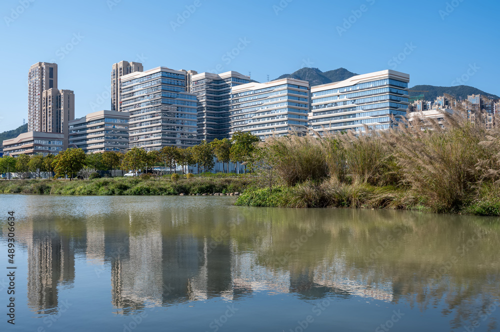 The river reflects the modern city buildings under the blue sky