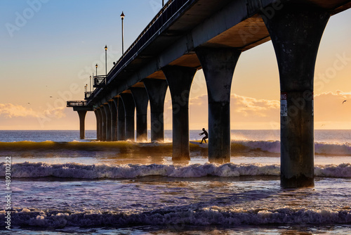 surfer riding through the pier at dawn