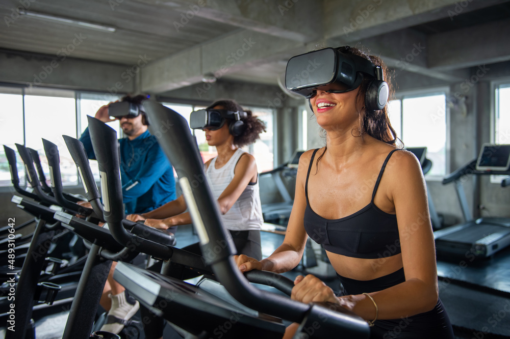 Fototapeta premium Healthy athletic man and woman wearing VR glasses workout exercise on cycling machine in virtual reality cyberspace at fitness gym. Metaverse digital entertainment technology and sport concept