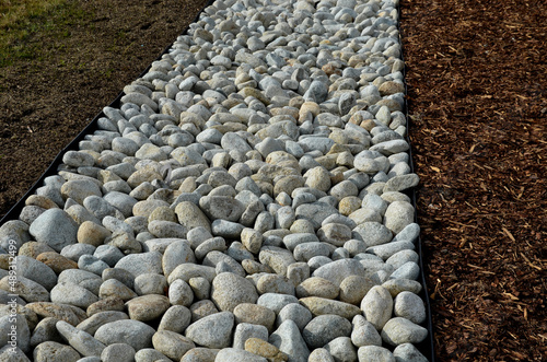The street line is planted in a rectangular strip mulched by large white pebbles. clearer and more formal appearance than mulch bark. clean representative of a park square with lawns, plastic curb