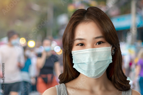 A close-up of a young Asian woman with smile under a sanitary face mask against coronavirus or COVID-19 at a street in an urban city. Virus and illness protection, sanitizer in a public crowded place