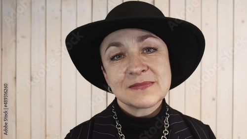Close-up portrait of a woman in a beautiful hat against a wooden wall. An elderly woman looks at the camera. High quality 4k footage