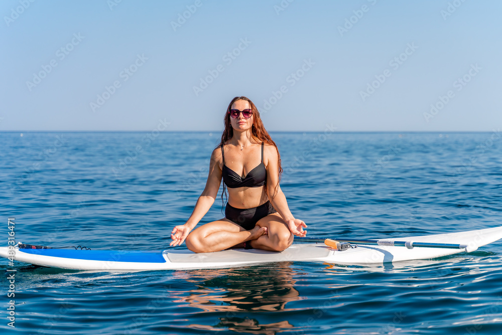 Sporty girl on a glanders surfboard in the sea on a sunny summer day. In a striped swimsuit, he sits in the lotus position with his eyes closed. Sporty girl on a glanders surfboard in the sea on a sunny summer day. In a striped swimsuit, he sits in the lotus position with his eyes closed.