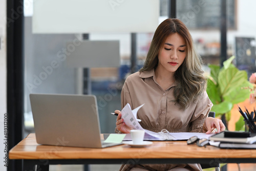 Concentrated young businesswoman checking financial reports and using computer laptop.