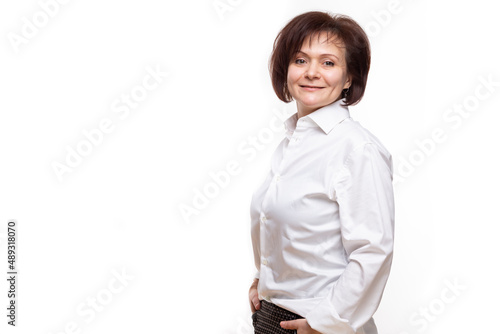 Portrait of Positive Mature Confident Caucasian Business Woman in White Shirt Posing With Hands In Pockets Over White Background.