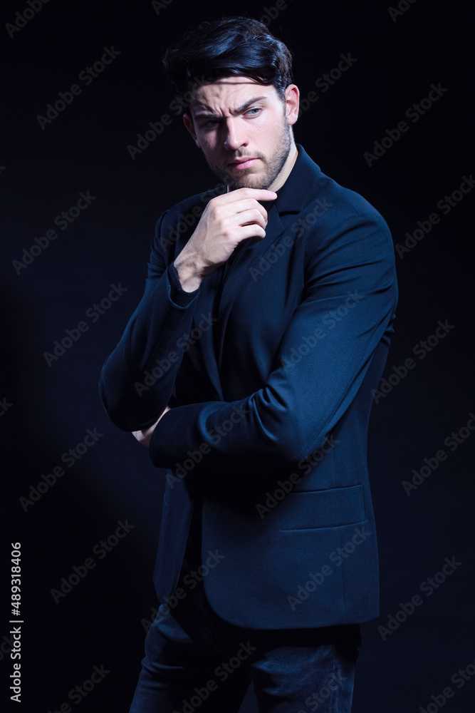 Thinking Caucasian Brunet Man In Black Suit Posing With Folded Hands Looking To Side Over Dark Background in Studio.