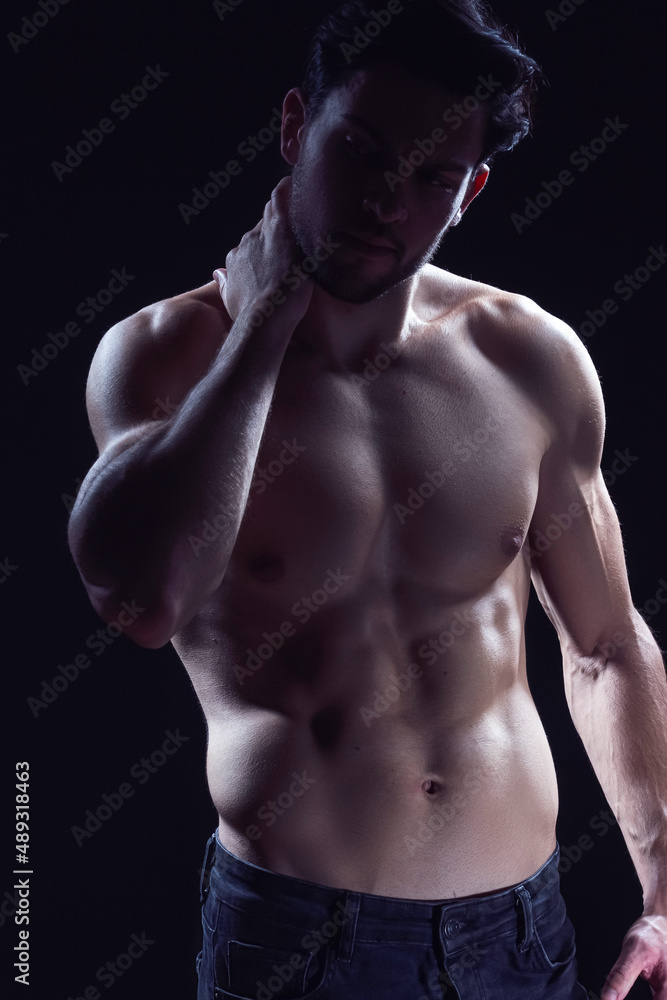 Fototapeta premium Youth Lifestyle. Contrast Portrait of Confident Thinking Caucasian Bodybuilder Athlete Man Posing With Lifted Hand With Naked Torso Against Dark