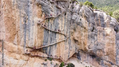Pasarelas de Montfalco at Congost de Mont Rebei Canyon, Catalonia and Aragon, North Spain - Aerial Drone View (Fly Back) of Tourists walking the Scary Stairs and Hiking Trail along the Steep Cliffs photo