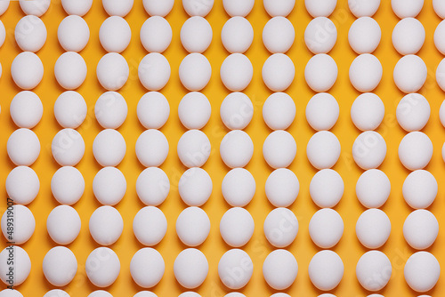 Pattern from white chicken eggs on yellow background top view. Creative food minimalistic background.