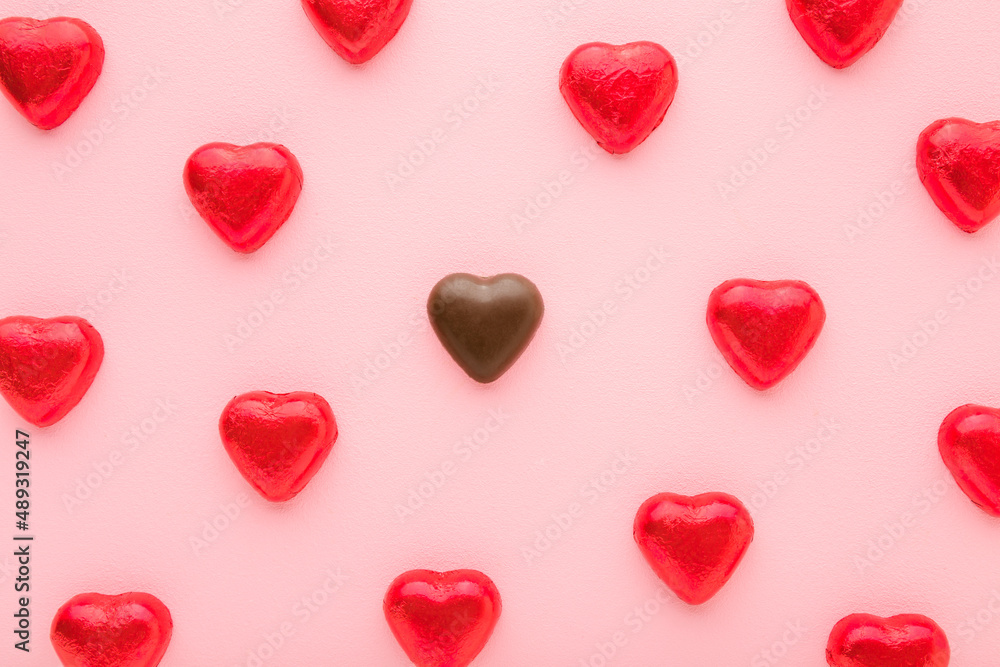 Heart shape chocolate candies wrapped in bright red foil paper on light pink table background. Pastel color. Love concept. Sweets pattern. Closeup. Top down view.