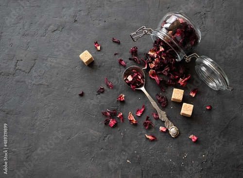 Dry petals of hibiscus tea scattered from a glass jar on a black background with space for text. Top view