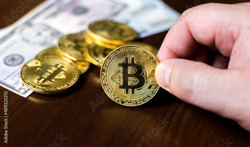 Man hands holding golden bitcoin, with american dollars in the background