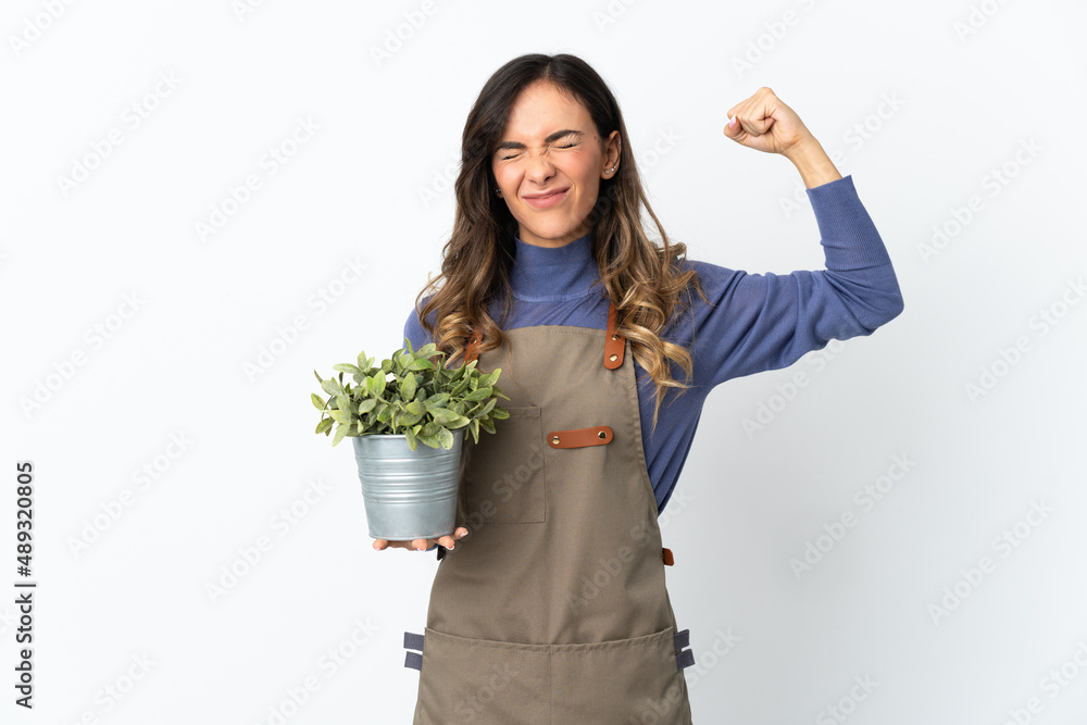 Gardener girl holding a plant isolated on white background doing strong gesture Gardener girl holding a plant isolated on white background doing strong gesture