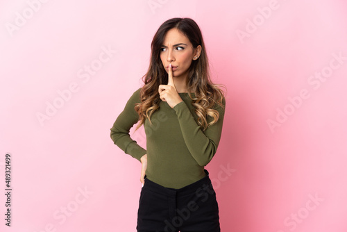 Young caucasian woman isolated on pink background showing a sign of silence gesture putting finger in mouth © luismolinero