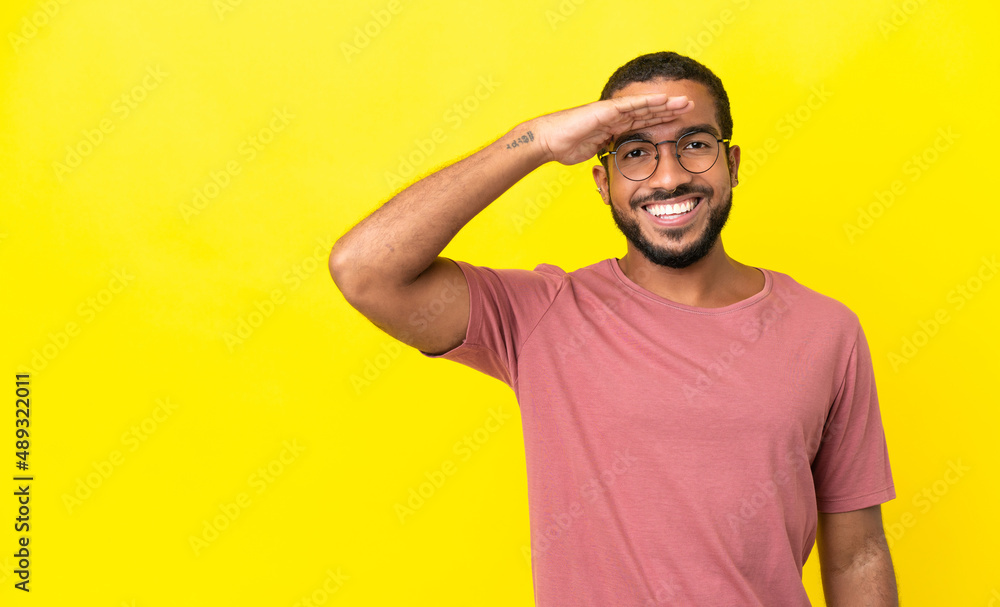 Young latin man isolated on yellow background saluting with hand with happy expression Young latin man isolated on yellow background saluting with hand with happy expression
