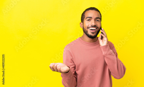 Young latin man isolated on yellow background keeping a conversation with the mobile phone with someone